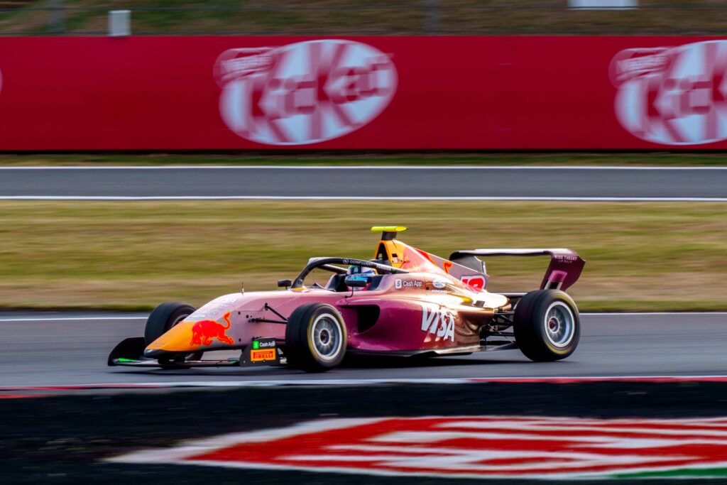 Rafaela Ferreira driving her pink and gold F1 Academy car at speed on track at Silverstone, motion blur panning shot